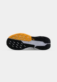 Semelle de chaussure de sport noire et orange avec des motifs de grip texturés, comportant une section blanche et le logo "Nike Trail" affiché en évidence.