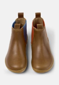 Botas de tobillo de cuero marrón con tiradores, panel lateral elástico azul en la bota izquierda y panel lateral elástico naranja en la bota derecha.
