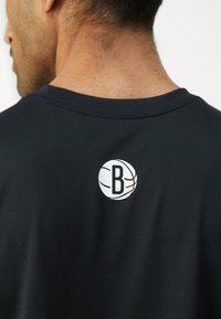 Svart bomullst-skjorte med en hvit basketball-logo med en 'B' på baksiden. Korte ermer og rund hals design. Glatt tekstur.