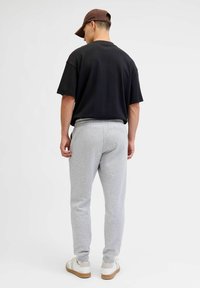 Czarny, oversizowy t-shirt, szare dresowe spodnie z elastycznym pasem oraz białe sneakersy z jasnobrązowymi podeszwami. Brązowa czapka noszona tyłem.