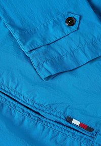 Helle blaue leichte Jacke mit Knopfverschluss, umgeschlagenem Ärmel und gesteppten Details. Beinhaltet einen dreifarbigen Logoakzent am Saum.