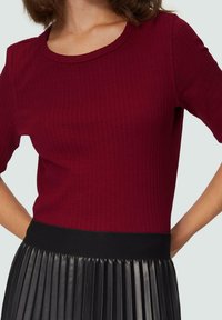 Top burdeos acanalado con cuello redondo y mangas cortas, combinado con una falda negra plisada que cuenta con una cinturilla suave.