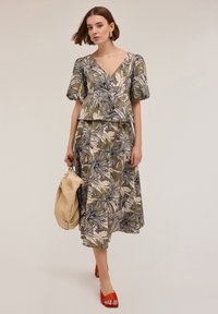 Completo due pezzi con stampa floreale in verde e beige, caratterizzato da maniche a sbuffo e una gonna svasata, abbinato a sandali rossi e una borsa beige.