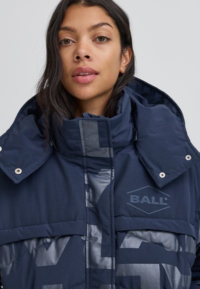 Tmavomodrá prešívaná bunda s vysokým golierom, lesklými akcentmi a logom. Tkanina má hladkú textúru s kontrastnými matnými a lesklými časťami.