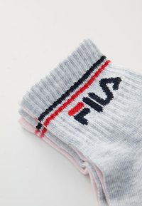 Graue Socken mit geripptem Textur, roten und schwarzen Streifen sowie schwarzem FILA-Logo. Weiches Material, oben umgeschlagen mit einem hellrosa Grund.
