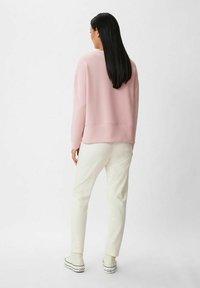 Jasnoróżowy sweatshirt o luźnym kroju, z długimi rękawami i ściągaczem, w połączeniu z białymi spodniami zwężanymi i białymi trampkami.