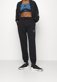 Black sweatpants with a drawstring, featuring a logo on the left thigh. Paired with a blue animal print sports bra and black bomber jacket.