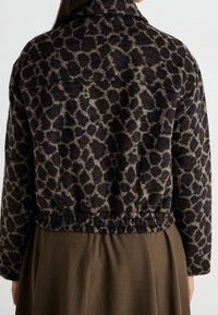 Jäck med leopardmönster i en kortad siluett, tillverkad av strukturerad tyg. Har krage och elastisk fåll. Bärs över en lång brun kjol.