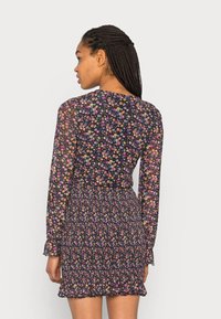 Vestido floral em tecido preto transparente, com uma estampa floral colorida, mangas longas, cintura franzida e bainha com babados.