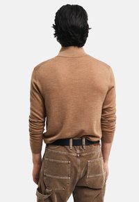 Suéter de lana marrón con un cuello corto, llevado por una persona que viste pantalones cargo color beige. Se aprecian la textura del tejido y el diseño ajustado.