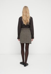 Camisa negra de manga larga; falda de tweed con estampado en negro, blanco y beige; medias opacas negras; zapatos negros; peinada con cabello rubio ondulado.