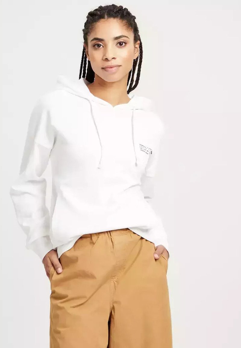 Biała bluza z kapturem i sznurkiem oraz przednią kieszenią, zestawiona z beżowymi spodniami. Materiał wydaje się miękki i ma luźny krój.