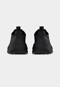 Paire de chaussures de sport noires vues de dos, avec des semelles épaisses et des languettes de traction, sur un fond clair uni.