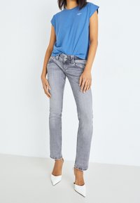 Camiseta azul de manga corta combinada con jeans gris ajustados y tacones blancos de punta. Los jeans tienen un diseño clásico de cinco bolsillos.