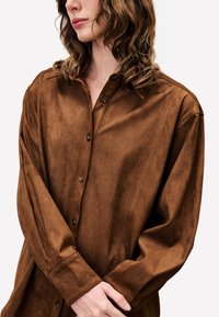 Brown button-up shirt made of soft suede-like material, featuring a collar, long sleeves, and subtle vertical seam details.
