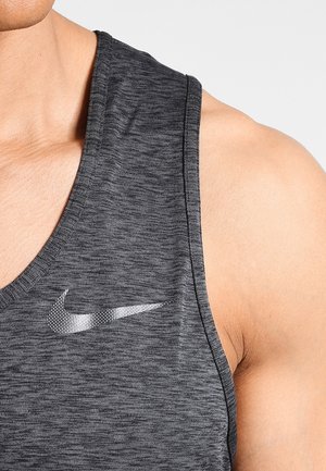 Zbliżenie na ramię i górną część klatki piersiowej w ciemnoszarej sportowej bluzce bez rękawów z białym logo Nike.