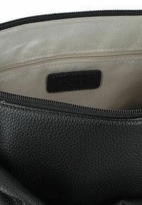 Interno di una borsa in pelle nera che mostra una superficie testurizzata e rigata, un rivestimento beige e una tasca con zip con un'etichetta nera.
