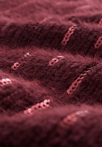 Bordo rdeč puhast material z bleščečimi rožnato zlati sequini, razporejenimi v vodoravne linije, ki ustvarjajo teksturiran videz z mehkimi, puhastimi nitmi.