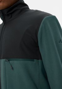 Giacca di pile con colletto alto, caratterizzata da un design color block verde e nero, pile testurizzato, tessuto liscio e una tasca con zip.