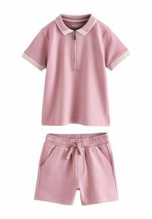 Rozā īss piedurkņu polo krekls ar baltām svītrām apkaklē un atbilstoši rozā elastīga vidukļa biksītēm ar aukliņu un sānu kabatām.