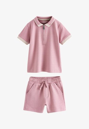 Tricou polo roz cu mâneci scurte și guler dungi albe, pantaloni scurți roz cu talie elastică, șnur de strângere și buzunare laterale.