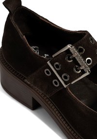 Braune Wildlederschuhe mit einem robusten Absatz, ausgestattet mit einem breiten Riemen mit Metallösen und einem silbernen Schnallen-Detail. Texturiertes Profil für besseren Halt.