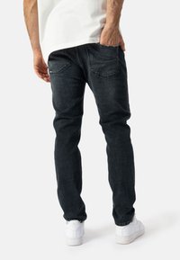 Tmavě modré džíny se slim fit, vybavené zadními kapsami a jemným whiskeringem na stehnech, spárované s bílými teniskami.