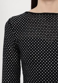 Zwarte trui met een gestructuurbreiwerk, versierd met zilveren rhinestones die in een rasterpatroon over de stof zijn aangebracht.