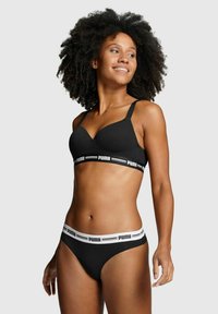 Schwarzer BH aus glattem Stoff, mit verstellbaren Trägern und einem breiten elastischen Bund mit weißem "PUMA"-Logo. Kombiniert mit passenden schwarzen Bikini-Höschen.