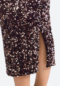 Pókhálós ruha sötét alappal, fényes bronzos flitterekkel, térd fölötti hosszúsággal és oldalsó hasítékkal a részletgazdagságért. Texturált felület, amely csillog.