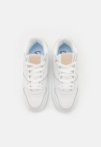 Baskets de sport blanches avec une boîte à orteils perforée, un intérieur bleu clair et des accents beiges ; elles présentent des lacets plats et une finition en cuir lisse.