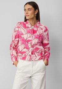 Veste à motif floral rose avec un design court, un col mandarin et une fermeture à boutons à l'avant. Assortie à un pantalon blanc à taille haute.