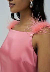 Top en satin rose avec des accents de plumes rose pâle sur les épaules et une petite épingle décorative. Texture lisse, décolleté carré.