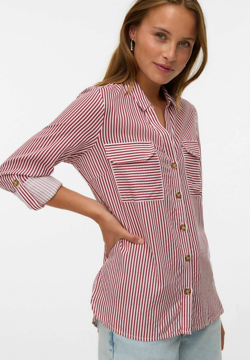 Camicia a righe rosse e bianche con due taschini frontali e maniche arrotolate, realizzata in tessuto leggero con una vestibilità comoda.