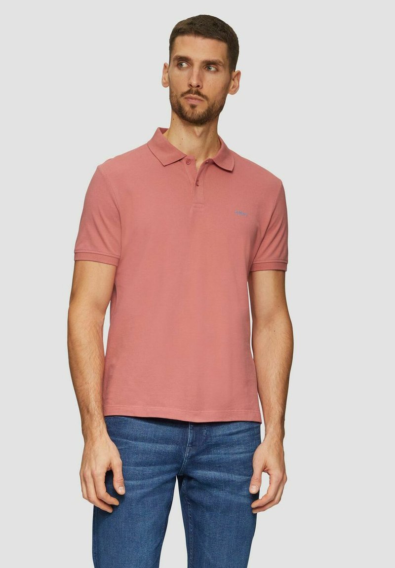 Rosa Polo-Shirt mit Kragen, kurzen Ärmeln und einem dezenten Logo-Detail. Kombiniert mit blauen Jeans; aus festem, strukturiertem Stoff.