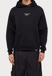 Czarna bawełniana bluza z kapturem. Posiada przednią kieszeń, ściągacze na rękawach i dole, z białym haftowanym logo na piersi.