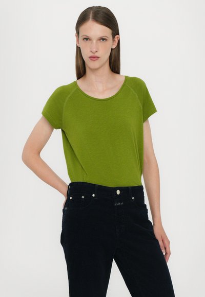 Green short-sleeve top with a round neckline and soft texture, paired with dark black jeans featuring front pockets and silver button accents.