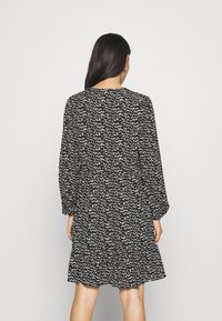 Mekko, jossa on musta-valkoinen kuvio, pitkät hihat, pyöreä pääntie ja kerroksellinen helma. Ominaisuuksiin kuuluu vapaa istuvuus ja pehmeä kangas.