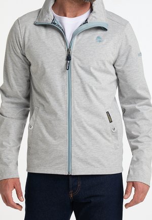 Mand iført lysegrå lynlåstrøje med to forlommer og blå lynlås over hvid skjorte, kombineret med mørkeblå jeans.