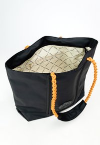 Czarna torba na ramię z plecionymi pomarańczowymi uchwytami. Otwarta wnętrze z jasnym podszewką w wzór oraz małą kieszonką na zamek.