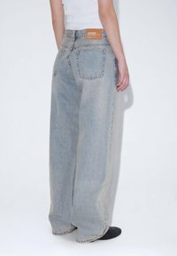 Ljusblå överdimensionerade denimjeans med en sliten textur, med en läderlapp i baksidan av midjan och två bakfickor.