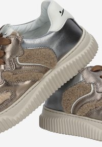 Baskets métalliques bronze et argent avec des panneaux en tissu beige texturé. Semelle épaisse en caoutchouc blanc avec des bords striés. Lacets et accents marron.