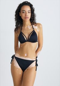 Juodas bikinis, kuris apima trikampį viršutinę dalį su keliais dirželiais ir reguliuojamais šoninės kaklono apatiniais. Lygus paviršius su minimalistiniu dizainu.