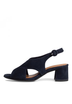 Marineblauwe suède sandaal met open teen, slingback ontwerp, lage blokhak en een sluitriem met een ronde gesp op een witte achtergrond.
