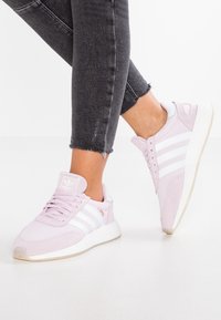 Ljusrosa Adidas-sneakers med vita ränder, gummisula och mjuk mockadikonsistens. Har snörning fram och vadderat ankelstöd.
