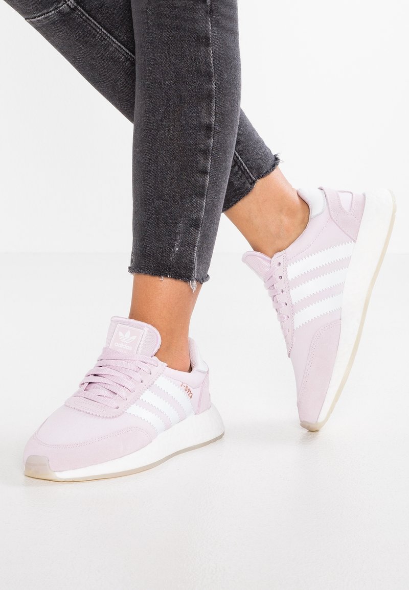 Ljusrosa Adidas-sneakers med vita ränder, gummisula och mjuk mockadikonsistens. Har snörning fram och vadderat ankelstöd.