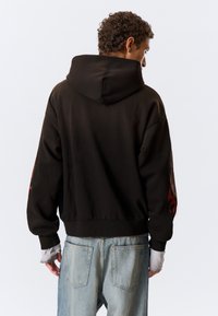 Sweat à capuche noir court avec une grande capuche, décoré de motifs de flammes rouges sur les manches. Le tissu semble doux, avec une coupe décontractée et un ourlet côtelé.