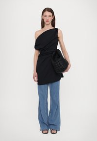 Zwart, één-schoudertop met gedrapeerde stof; gecombineerd met lichtblauwe flared jeans en een zwarte gevlochten handtas; gedragen met zwarte sandaaltjes met bandjes.