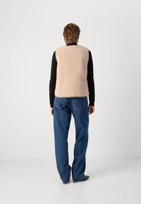 Γούνινο γιλέκο σε ανοιχτό μπεζ με μαλακή υφή. Διαθέτει στρογγυλή λαιμόκοψη και καμπυλωτό τελείωμα. Συνδυάζεται με μπλε ίσιες τζην παντελόνες.