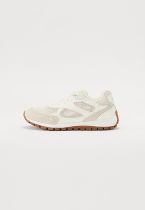 Šviesiai smėlio spalvos sportinė avalynė su akių panelėmis, zomšos detalėmis ir gumine pado dalimi. Batai turi apvalų noselį ir paminkštintą apykaklę komfortui.